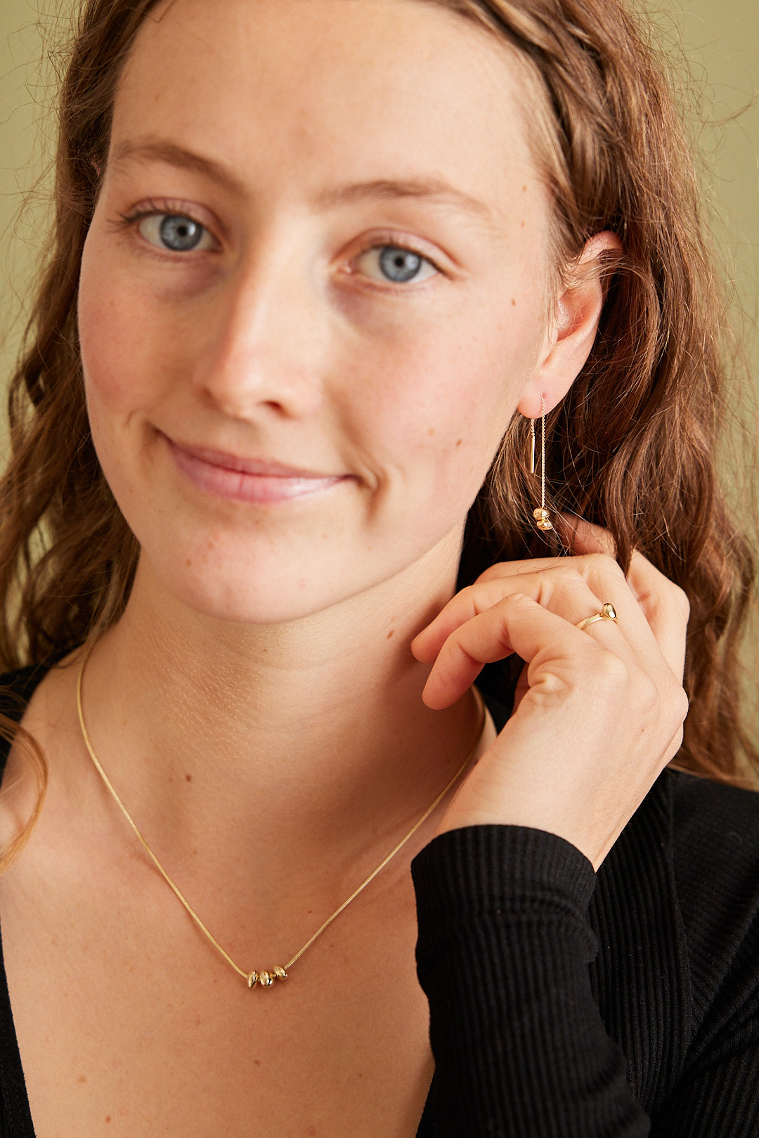 Model draagt gouden sieradencollectie Essentials, bestaande uit ketting, oorhangers en ring met gouden steentjes