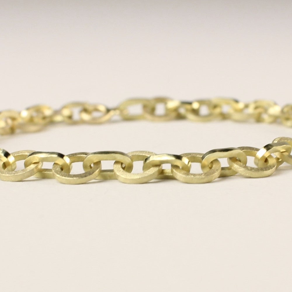 Close-up van Unieke 14 karaat gouden schakelarmband met matte ronde schakels afgewisseld met hoogglans ovale schakels. Slechts een van gemaakt. Liggend op een witte achtergrond.