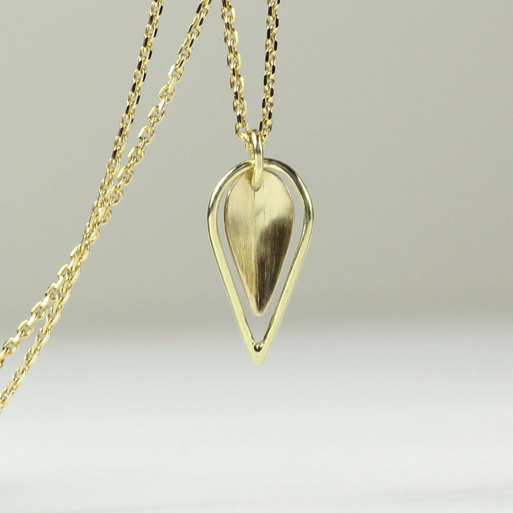 Dubbel hangertje Leaves, minimalistisch gouden blaadje met daaromheen een open blaadje gemaakt van gouddraad als omlijsting. Getoont op witgrijze achtergrond, hangend aan een gouden ketting.