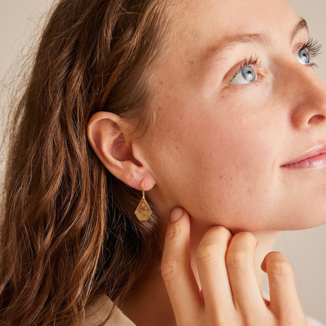 Zijaanzicht van het gezicht van een model met 18 k gouden oorhangers Imperfectie Rocks in.