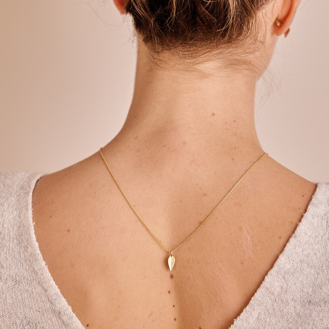 Model draagt achterstevoren een 14 k gouden hanger Leaves, een minimalistisch blaadje.