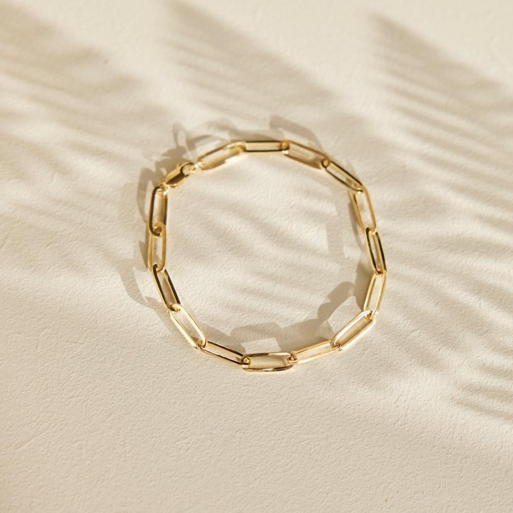Verbondenheid paperclip armband. 14 karaat schakelarmband liggend op een zandkleurige ondergrond in de schaduw van een varenblad.