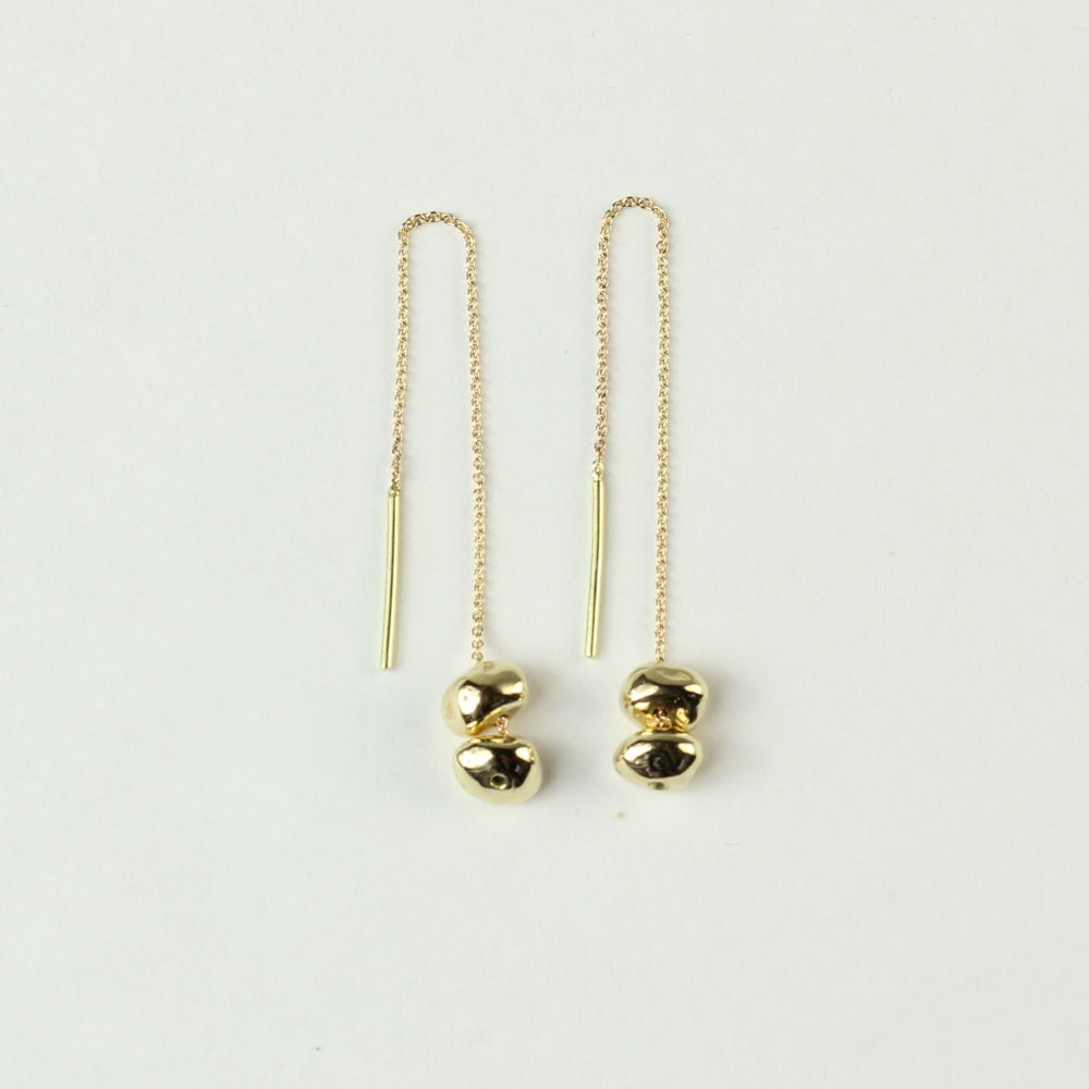 Doorrijgoorbellen Oorhangers Essentials: 14 k gouden minimalistische steentjes aan een kettinkje welke je door je oren kan trekken. Liggend op een witte achtergrond.