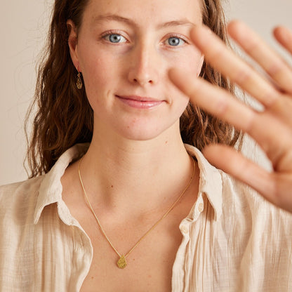 Model draagt ketting en oorbellen met 18 karaat gouden "Imperfectie Rocks". Van gezicht tot borst in beeld met hand vooruit gestoken.